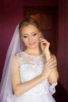 Portrait of beautiful bride with fashion veil posing on bed at wedding morning. Makeup. Brunette girl with long wavy hair styling. Wedding dress.