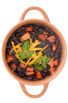 Bowl of nutritious black bean soup garnished with cheddar cheese, fresh parsley and tomato viewed close up from above isolated on white