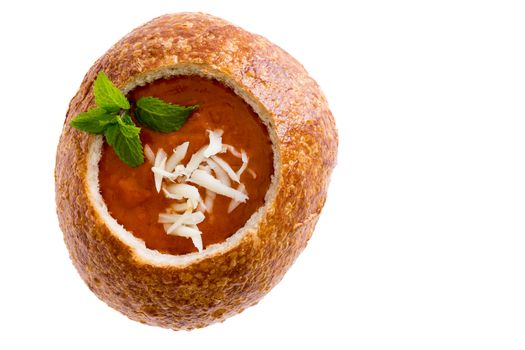 Isolated tomato soup garnished with grated cheese and fresh herbs served in a crusty sourdough bread bowl viewed from above on white with copy space
