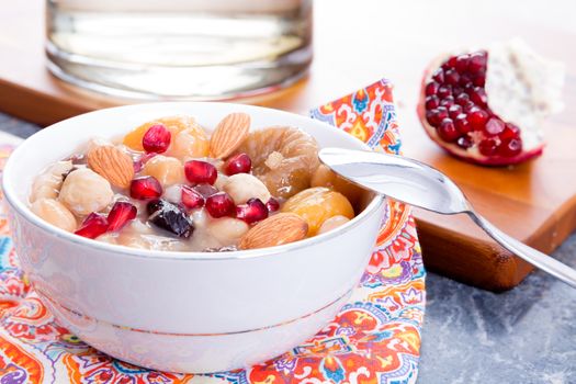 Turkish Noah's Pudding or ashure served with pomegranate and nuts in a white bowl on a colorful napkin for dessert
