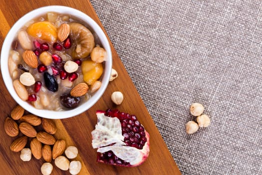 Noah's food or ashure, a speciality Turkish sweet grain pudding, served with hazelnuts, almonds and pomegranate seeds, overhead view with ingredients and copy space on textured beige linen