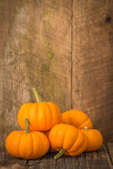 Small pile of ripe pumpkins on a weathered, rustic wooden background.