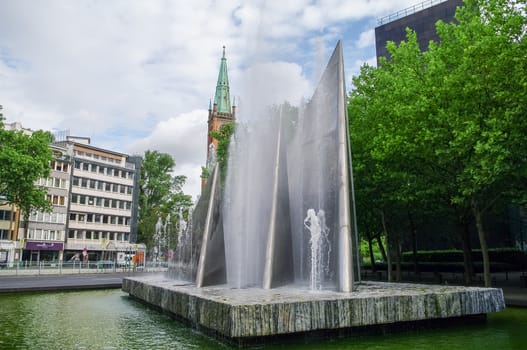 Fountain in German Reunification Memorial Square and Protestant Church Saint Johns (Johanneskirche) at background, Dusseldorf, Germany
