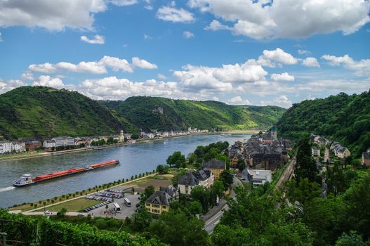 Panoramic view of Sank-Goar and Snak Goarshausen medival village and Rhine vineyards on slope of the hills in Germany. Cargo ship sails on the Rhine river.