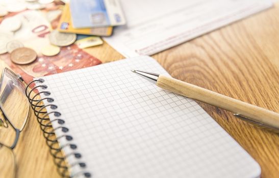 Conceptual image for planing and organizing the financials with a graph notepad, pen, eyeglasses and money, cards and bills in the background.