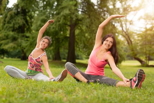 Two beautiful women doing stretching exercise in the park. 