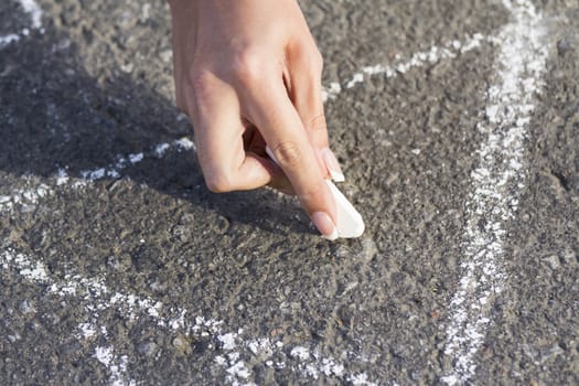 Hand girl draws by a chalk roof House on the sidewalk