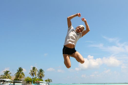  an jumping happy in the beach with a blue sky and palms in the background