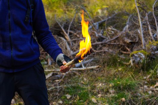 Man hand with torch and flame in wild nature background.
