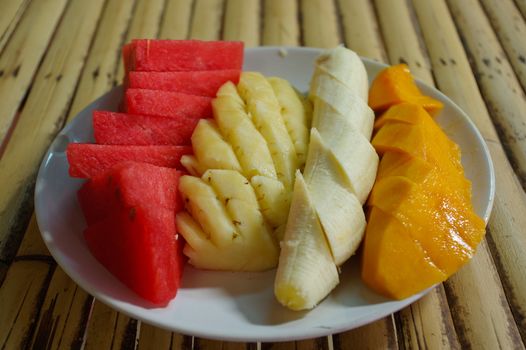 a white plate with sliced fruit: watermelon, mango, banana, pineapple. on the table in a cafe.