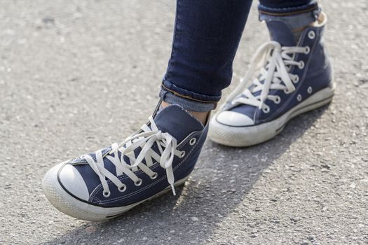 Close-up of female feet in fashionable sneakers are standing on the sidewalk