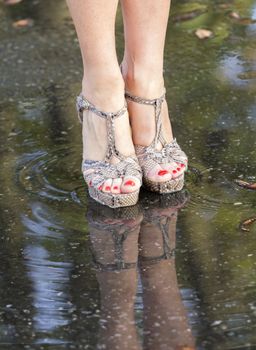 Women's legs in fashionable shoes and their reflection in a puddle.