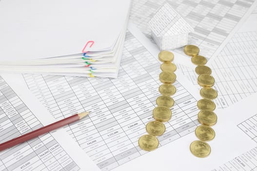 Pile of gold coins place as way to home on finance account have pencil and blur pile overload paperwork of report and receipt with colorful paperclip as background.