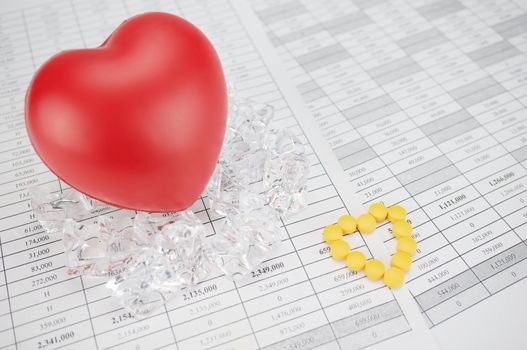 Yellow pills place as heart shape on finance report have blur red heart on stack of ice as background.