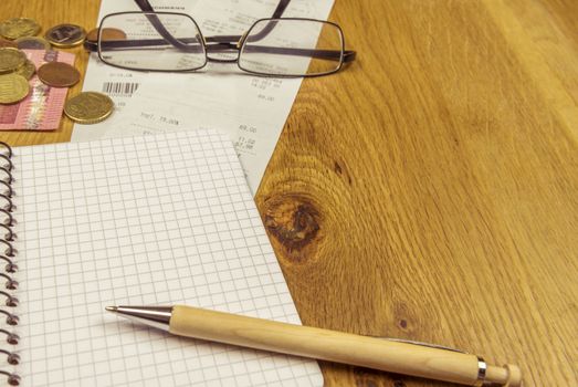 Office desk with an opened graphic notebook, a pen, some euro coins, bills and a pair of glasses