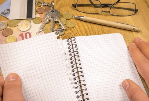 Conceptual image with a man's hand tearing a blank page from a spiral math notebook, money, keys and credit cards in the background.