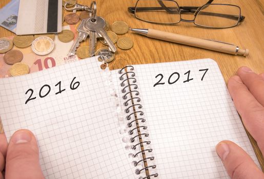 A man's hands tears a page from a notebook with the year 2016 written, remaining the page with the 2017 year. Financial elements in the background and copy space.