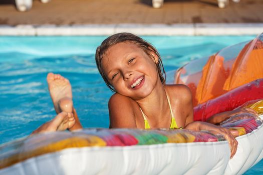 Little girl on inflatable mattress in swim pool. Smiling child playing and having fun in swimming pool with air mattress. Kid playing in water. Summer vacations concept.