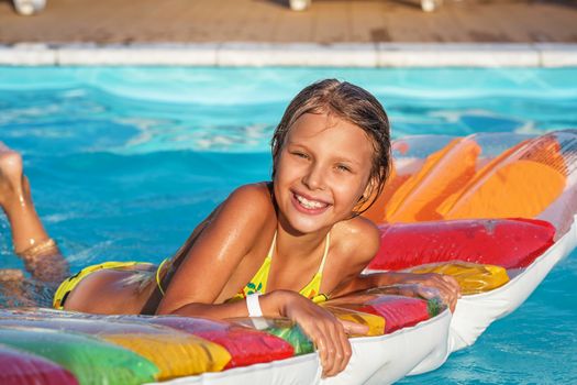 Little girl on inflatable mattress in swim pool. Smiling child playing and having fun in swimming pool with air mattress. Kid playing in water. Summer vacations concept.