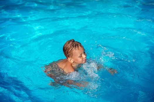 Happy kid playing in blue water of swimming pool. Little boy learning to swim. Summer vacations concept. Cute boy swimming in pool water. Child splashing and having fun in swimming pool