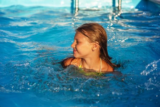 Happy kid playing in blue water of swimming pool. Little girl learning to swim. Summer vacations concept. Cute girl swimming in pool water. Child splashing and having fun in swimming pool