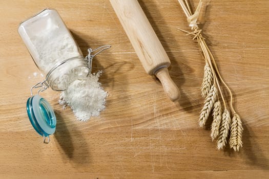 Flour in glass jar on a table with rolling pin and sheaves of wheat from above