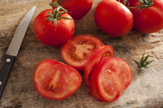 Sliced succulent red tomatoes beside serrated knife and other uncut ones on a rustic wooden table