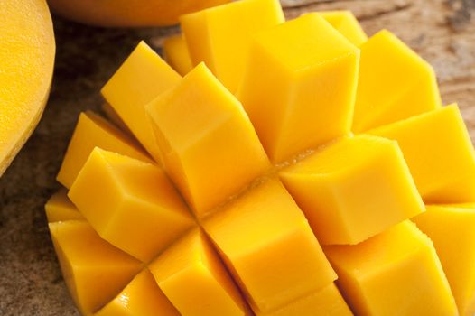 Delicious yellow mango peeled and cut into squares beside other ones on a wooden rustic table