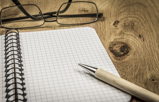 Graphic spiral notebook with copy space and eyeglasses on wooden desk, in vintage settings