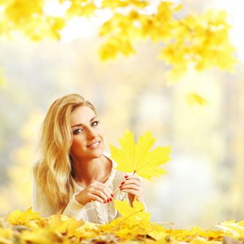 Happy young woman laying on autumn leaves in park