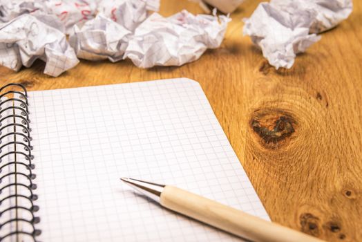 Math spiral notebook  with a pen on it and thrown crumpled pages in the background, on a wooden desk.