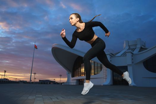 Concept: healthy lifestyle, sport. Attractive happy girl fitness trainer run outdoor workout at modern downtown urban area during sunset.