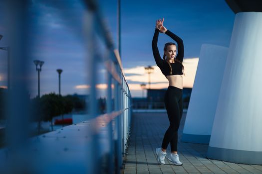 Concept: healthy lifestyle, sport. Attractive happy girl fitness trainer do outdoor workout at modern downtown urban area during sunset.