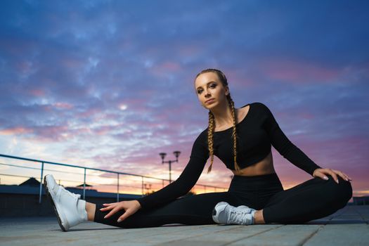 Concept: healthy lifestyle, sport. Attractive happy girl fitness trainer stretch outdoor workout at modern downtown urban area during sunset.