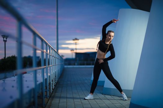 Concept: healthy lifestyle, sport. Attractive happy girl fitness trainer do outdoor workout at modern downtown urban area during sunset.