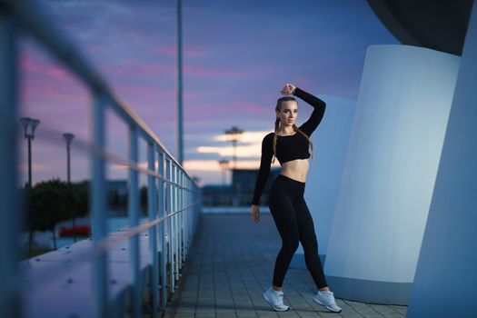 Concept: healthy lifestyle, sport. Attractive happy girl fitness trainer do outdoor workout at modern downtown urban area during sunset.