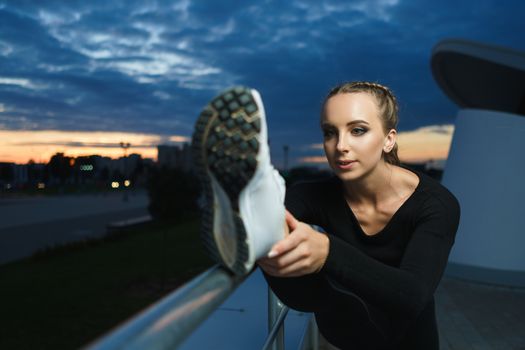 Concept: healthy lifestyle, sport. Attractive happy girl fitness trainer stretch outdoor workout at modern downtown urban area during sunset.