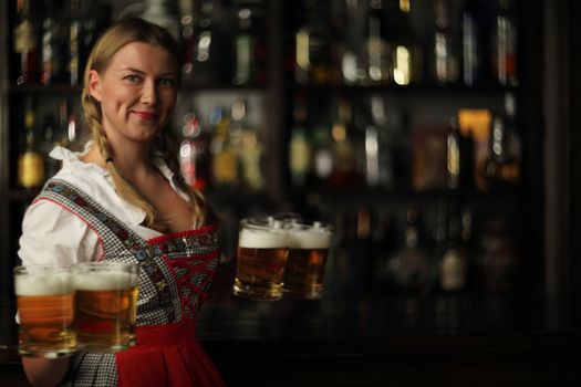Pretty oktoberfest blonde woman holding beer mugs in bar