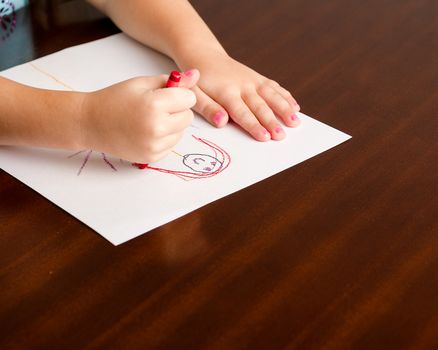 Image of a childs hands, a crayon, and paper on a table while she is creating her masterpiece