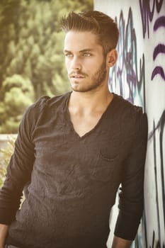 Attractive young man leaning against colorful graffiti wall, looking at camera