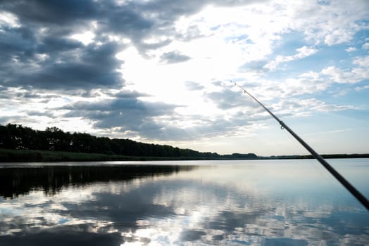 Fisherman sport hobby fishing rod or spinning reel on the river. Fishing on sunrise. beautiful sunrise on the river is reflected in water.