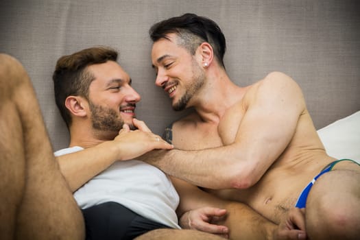 Handsome men lying on bed together while looking face to face with smile