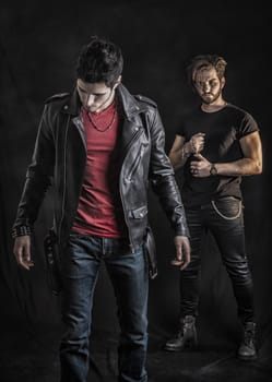 Two attractive young hard rock men posing in studio. Black background