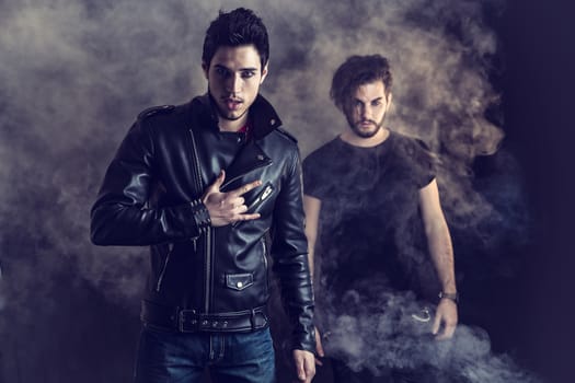 Two attractive young hard rock men posing in studio. Black background