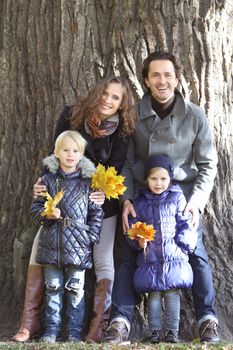 Happy family in autumn park near big tree trunk