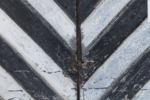 Detail of an old wooden gate with black and white stripes, creating a letter "V" or an arrow.