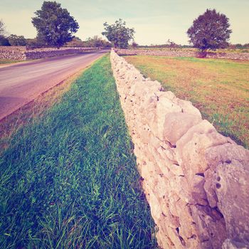 Asphalt Road along the Pasture Divided into Section by the Stone Wall, Vintage Style Toned Picture