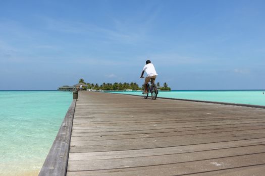 a man rides a bicycle on a wooden bridge in the direction of an Maldievs island