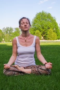 a young woman sitting in yoga lotus pose meditation outdoors