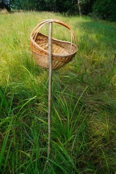 a closeup picnic basket hanging on a rod in grass, outside with green nature background